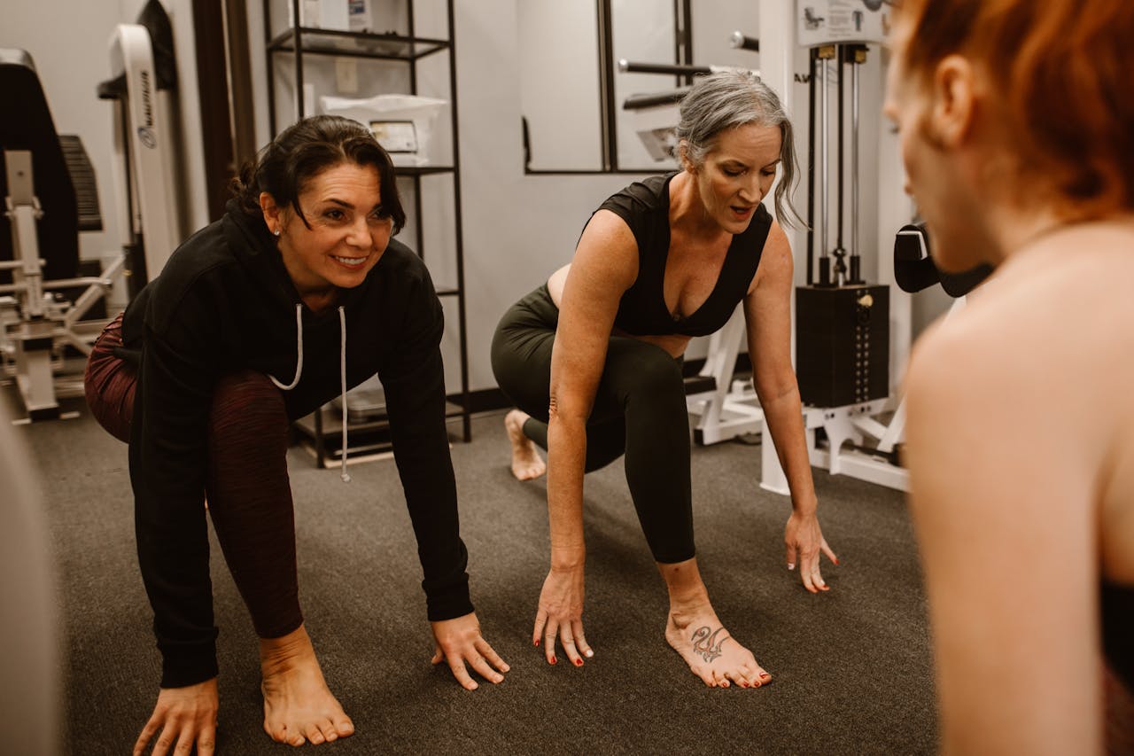 heros-img Three women engaged in a workout session in a gym, focusing on strength and balance.